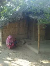 A Rohingya woman crouches next to a small boy in front of a bamboo structure. 