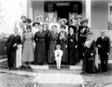 A black-and-white photograph of 17 women, two men and a child posing on the front steps of a house. All are dressed in early twentieth-century clothing.