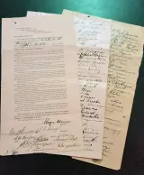 A close-up of an original French-language petition with two pages of signatures fanned out behind it.