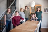 A smiling family of six gathered around a dining room table. 