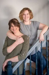 One woman and one trans man embracing affectionately and smiling at the camera.