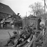 A group of armed soldiers watch a tank drive past.
