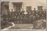 A nun and a group of First Nations children in school uniforms posing in front of a stone building.