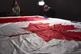 Two women wearing protective gloves and aprons working around a large Canadian flag, which lies flat on a table.
