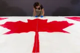 A woman wearing protective gloves and an apron takes notes behind a Canadian flag, which lies flat on a table in the foreground.
