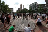 People in a town square stand and kneel around a large display of coffee cups laid out on the ground.