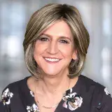 A woman in a flowered top looks at the camera.