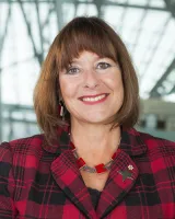 A white-appearing woman with short brown hair wearing a red and black checkered blazer.