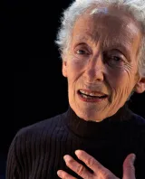 A woman with short, white hair faces the camera. 