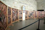 Left view of a structure of vertical wood panels covered in patterns of images, with a white wooden door at the centre.