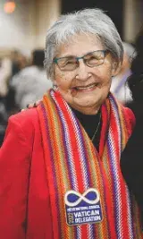 Une femme aux cheveux gris courts porte un foulard multicolore sur les épaules et un blazer rouge.