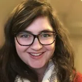 White woman with brown hair, brown eyes and dark rectangular glasses.