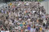 A very large crowd of people filling a wide street, marching. Many carry signs with slogans such as “Don’t touch me,” “Abusers deserve consequences” and “No means no.”