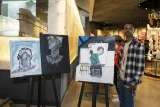 In a museum gallery, a student stands beside three paintings that they've created.