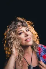 A woman with blond curly hair looks flirtingly at the camera.