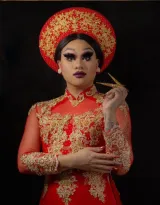 A drag artist is wearing Vietnamese cultural clothing with a matching red and gold headdress and long dress.
