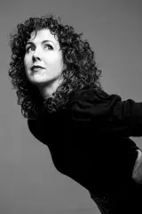A black-and-white headshot of a woman with curly, shoulder-length hair.