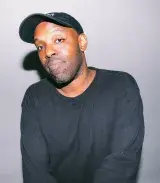 A black man wearing a dark grey cap and long-sleeve shirt.