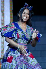 A black woman wearing traditional African dress is smiling and dancing.