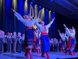 An ensemble of Ukrainian performers dancing on stage; those in the front are looking and reaching up with their arms.