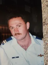 A young man in a white military uniform with blue epaulets on the shoulder gazes seriously ahead.