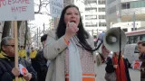 A woman holding a microphone attached to a bullhorn at a protest on a city street.