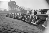 Black-and-white photograph of a row of cars parked in a field. 