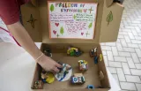 An open cardboard box with a scene of people interacting made of clay. 