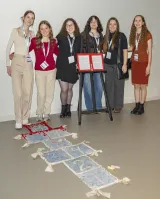A group of girls stand behind a game of hopscotch. The last few squares have red on them, resembling blood.