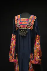An intricately designed necklace hangs around the neck of a dark blue dress with patterns in red, blue and yellow on the sleeves, chest and sides and neckline.
