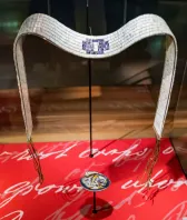 A white-and-blue belt made of shells is displayed on a stand.