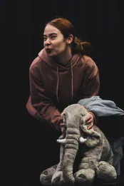 A woman is bent over and squeezing the head of a large toy elephant between her hands