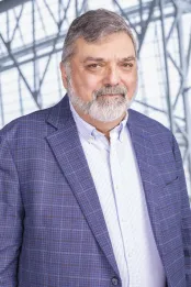 A man with grey hair wears a blue-purple blazer with a white shirt.