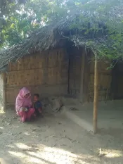 A Rohingya woman crouches next to a small boy in front of a bamboo structure. 