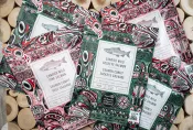Packages with colourful Haida-themed designs sit in a pile. The large text on the packages reads “Candied Wild Sockeye Salmon” or “Candied Wild Pink Salmon”. Smaller text reads “Oncorhynchus nerka” , “60g”, “ready to eat”, “sustainable”, and “Authentic Indigenous Seafood”