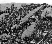 Aerial photo of a long line of coffins surrounded by a large crowd of people. 