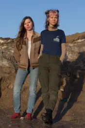 Deux jeunes femmes blanches se tiennent debout, les mains dans les poches, dans l’eau de fonte d’un tas de neige sale. Leurs expressions et leurs postures sont très décontractées.