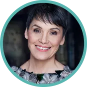 A woman with short dark hair and a blouse with a collar of flowers smiles.