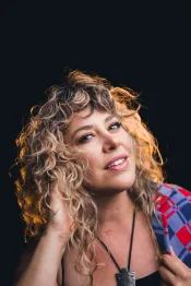 A woman with blond curly hair looks flirtingly at the camera.
