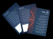 Three cards lay flat on a black table. Each card has the poem “Think of Others” by Mahmoud Darwish printed on it. The card on the left has the poem translated in French. The card in the centre has the poem translated in English. The card on the right in full view has the original poem written in Arabic.