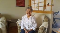 Lena Hayakawa sits in a chair an smiles at the camera. She is wearing a white blouse and black pants.