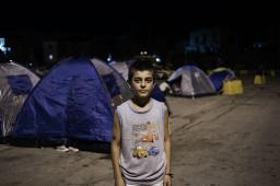 A teenage boy stands in front of tents in a parking lot at night.