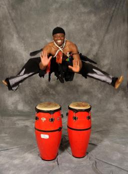 A person leaps in the air above conga drums.