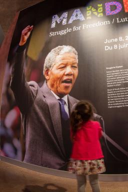 A young girl looks up at a large photograph of a man holding his fist in the air on the title panel for a museum exhibition.