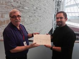 Two men standing in front of a stone wall in the Museum holding a handwritten document.