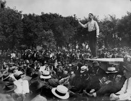 A man on a raised platform addresses a large crowd.