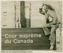 A man sitting on a sign that reads “Supreme Court of Canada” in French clasps his hands over his head in a symbol of victory.