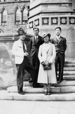 A black-and-white image of three men and one woman standing on a set of stone steps.