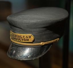 Black cloth cap with a badge on the front reading “sleeping car conductor.”