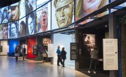 People look at rows of Museum exhibits. There are large images in a grid overhead.